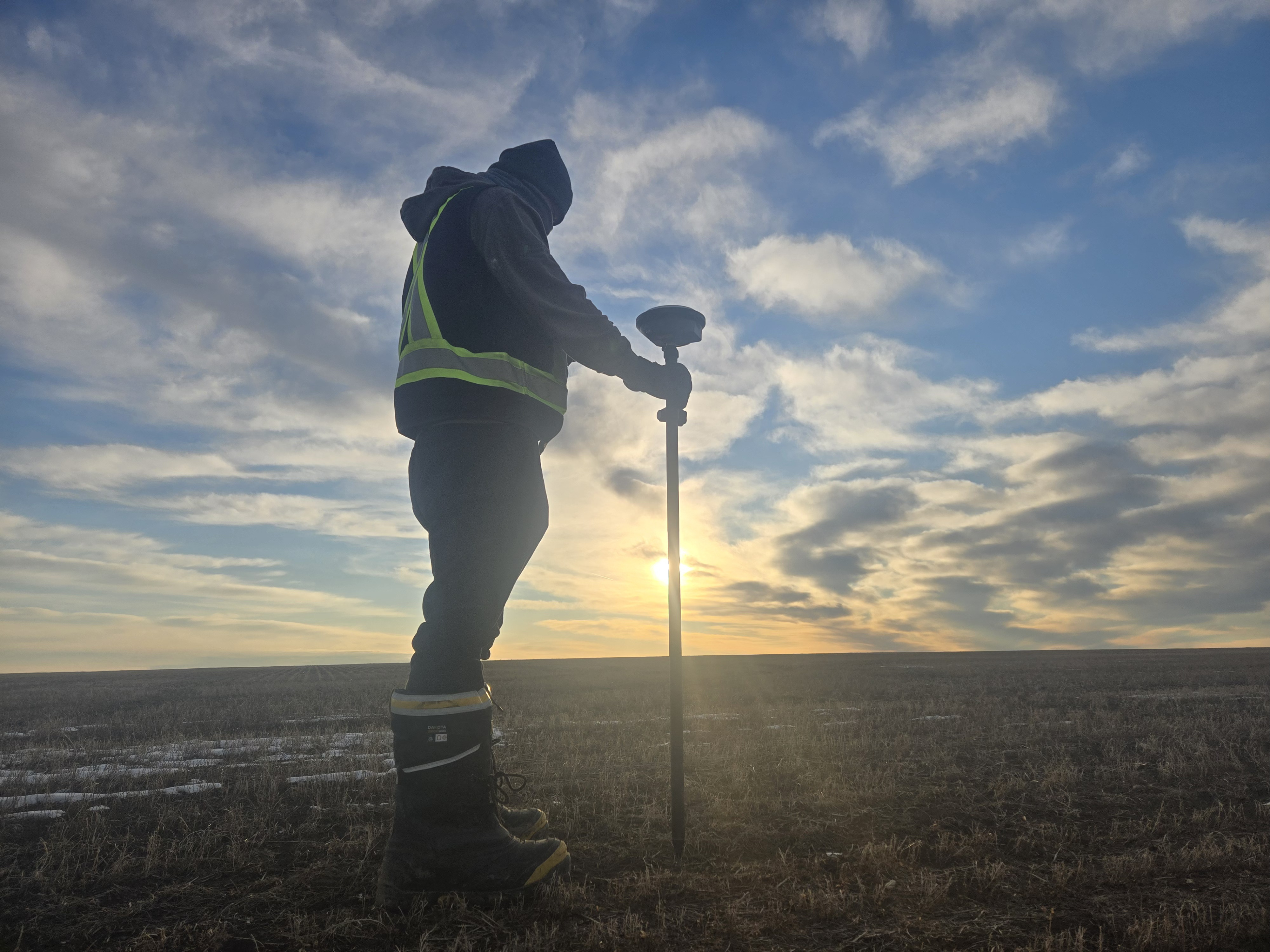 Surveyor with GNSS rover at sunset