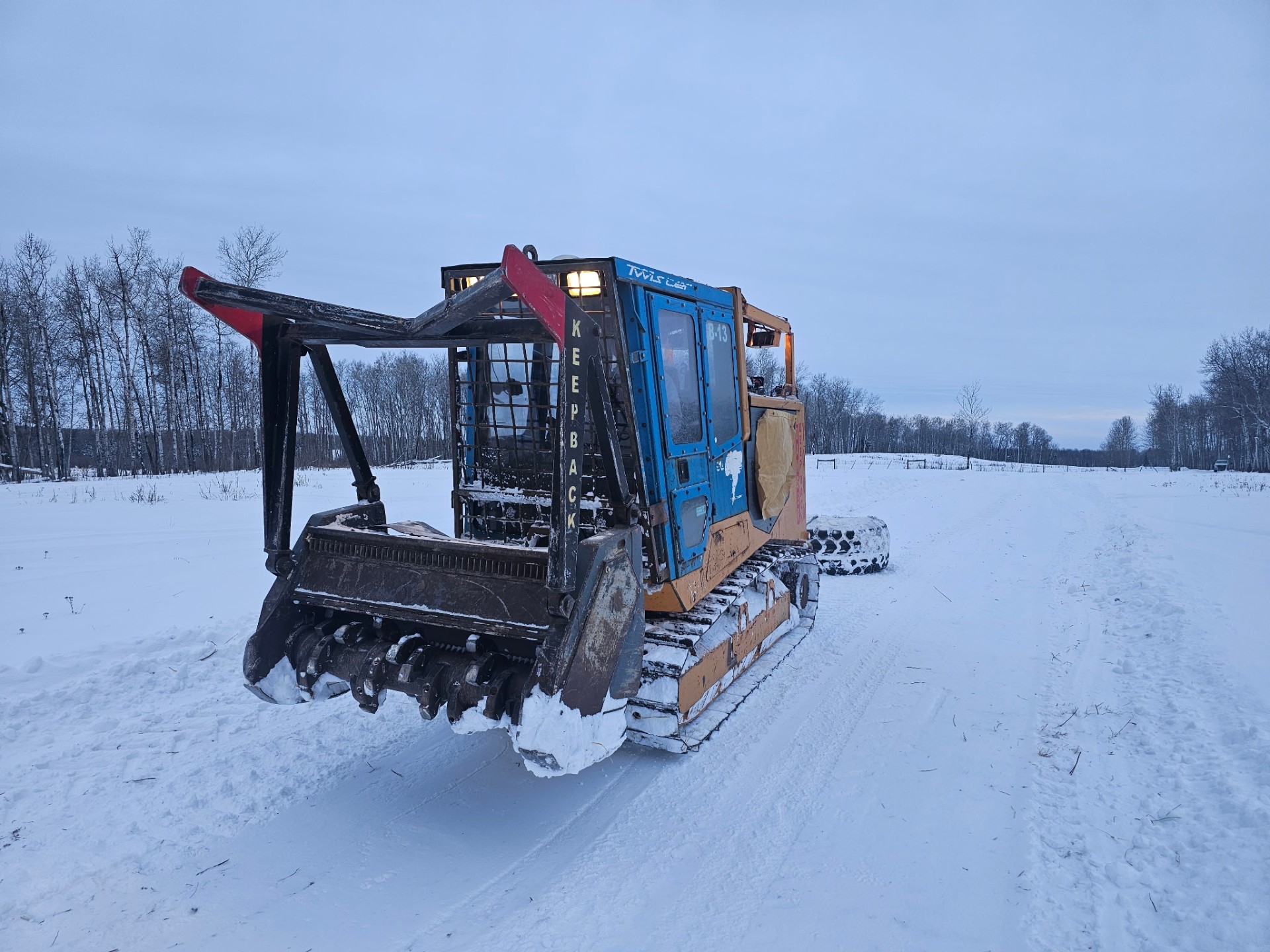 Single mulcher parked on a snow-covered access road at dawn