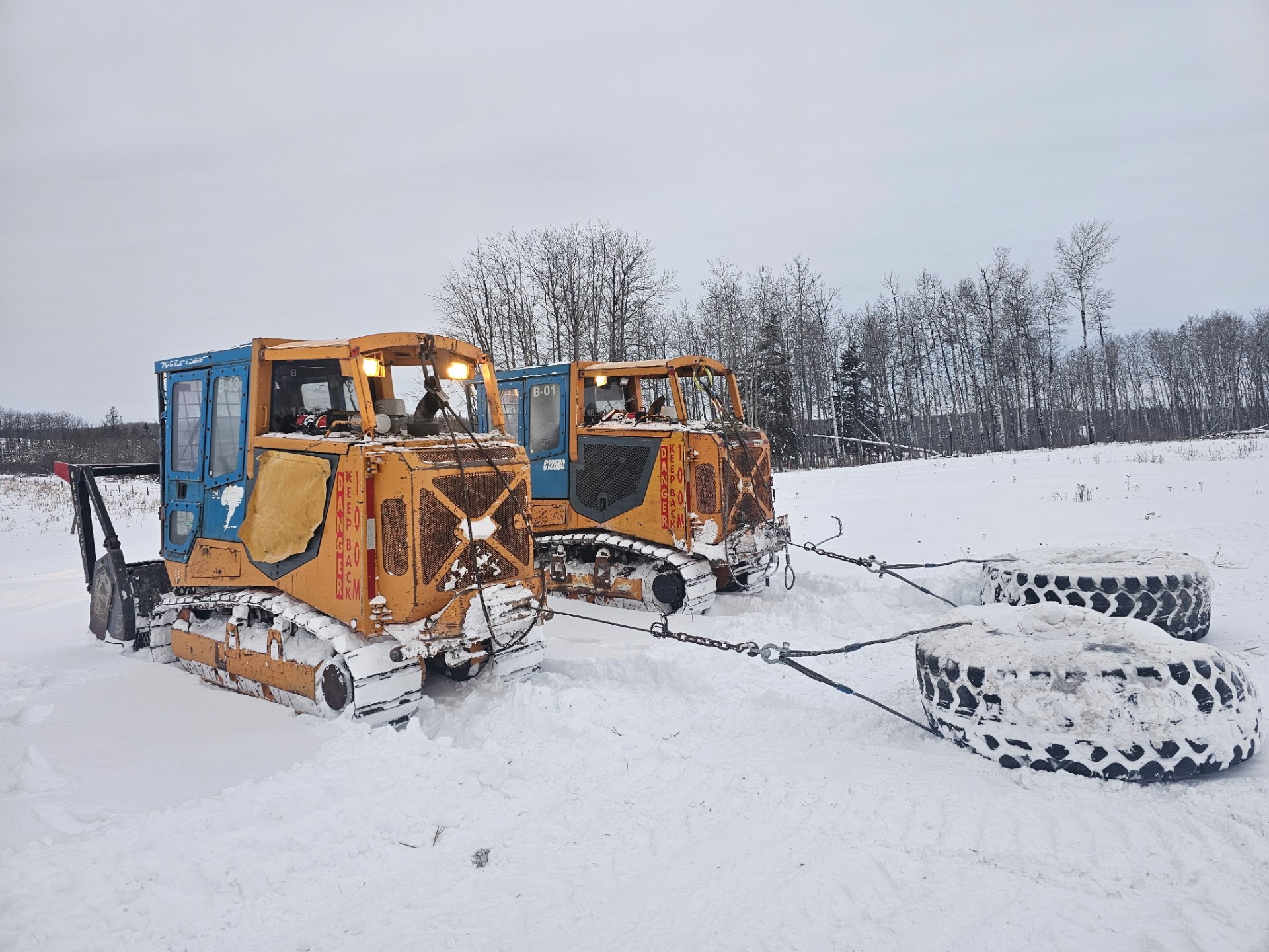 Side angle of two mulchers towing tire drags in snow