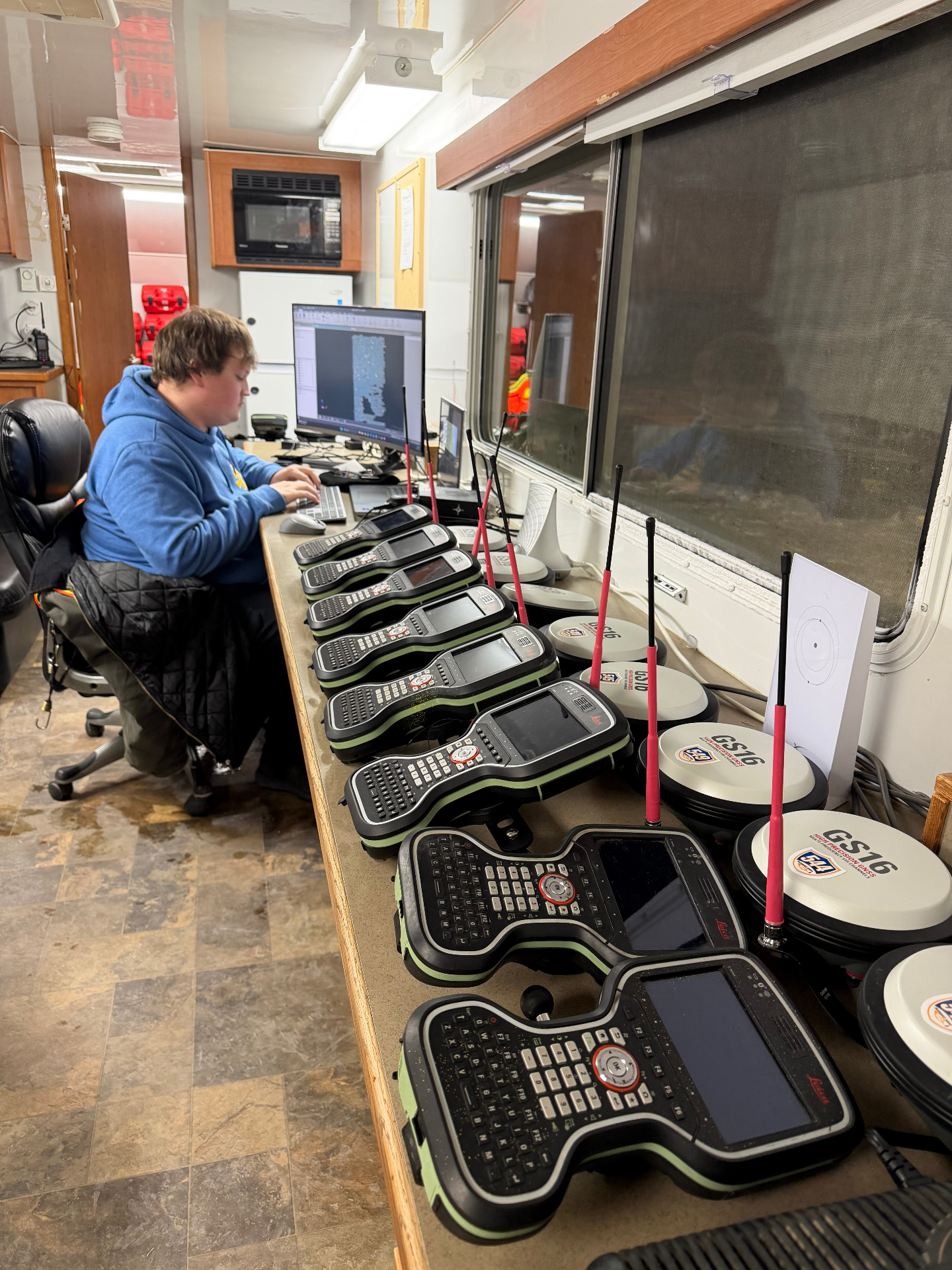 Technician processing GNSS data beside a row of Leica controllers and GS16 receivers